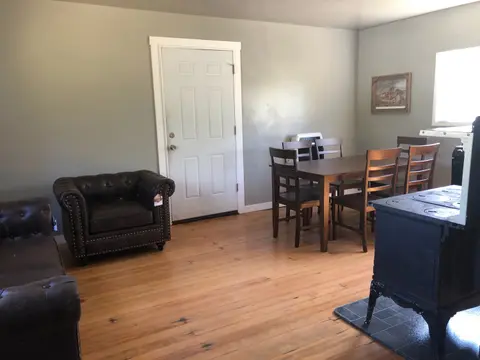 An interior shot of a room with a wooden floor, a dining set, and leather furniture.