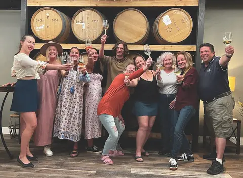 A group of people holding up glasses of wine in front of wine barrels.
