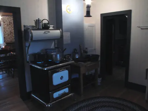 A vintage kitchen interior features a wood and gas stove with pots and pans.