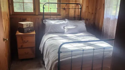 A bedroom with a metal bed frame, wooden panel walls, and a nightstand with suitcases on it.