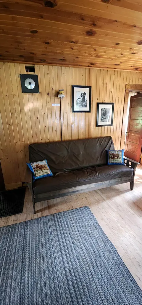 A wooden interior room with a futon sofa against a wood-paneled wall.