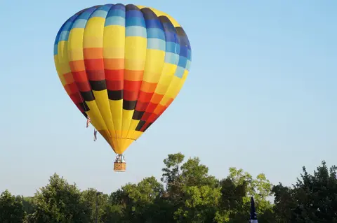 A colorful hot air balloon flies above green trees.
