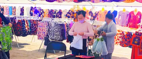 A woman stands behind a clothing rack at an outdoor market.