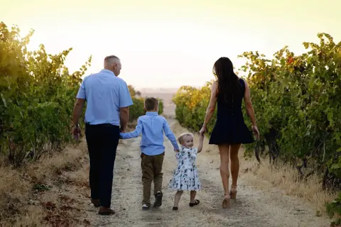 A family walks together down a dirt path between rows of grapevines.