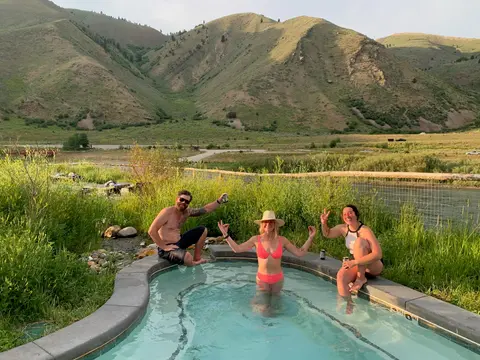 Three people enjoying a natural hot spring pool with mountains in the background.