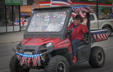 A woman waving from a decorated utility vehicle in a parade.