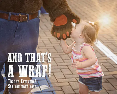 A toddler kisses a mascot's paw outdoors.