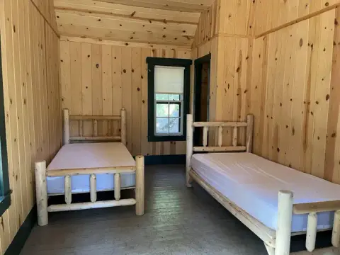 A small room with two wooden log beds and pine-paneled walls.