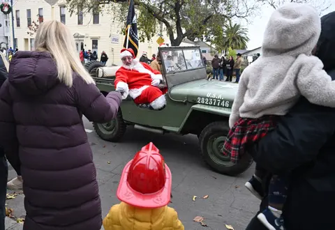 Santa Claus waves from a military jeep during a parade.