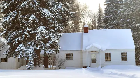 A white house covered in snow surrounded by snowy trees.