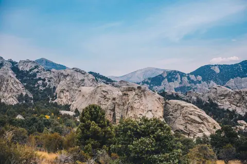 A scenic landscape featuring rocky mountains and trees under a blue sky.