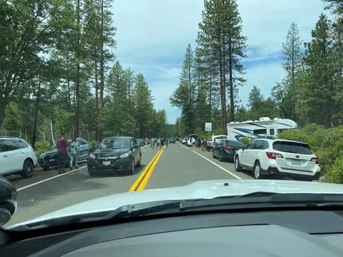 A view from inside a car looking down a two-lane road lined with parked cars and trees.