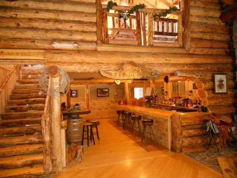 An interior view of a rustic log cabin bar and staircase.