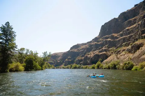People float down a river surrounded by rocky cliffs and trees.