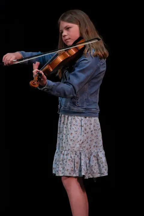 A young girl playing the violin against a black background.