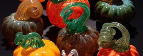 A collection of colorful glass pumpkins sits on a dark surface.
