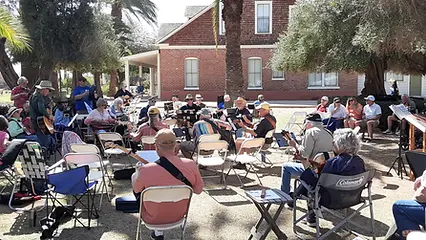 A group of people sitting outdoors playing musical instruments together.