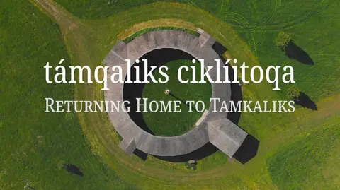 An aerial view of a circular wooden building in a grassy field.