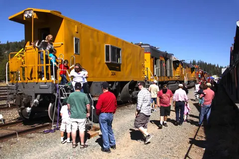 People board and walk alongside a yellow train.