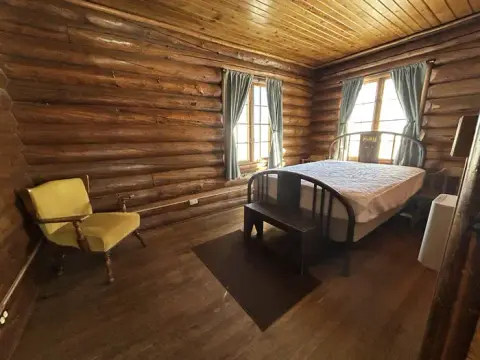 A rustic bedroom with log walls, a wooden floor, a bed, and a yellow chair.
