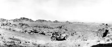 A vintage car parked on a dirt road in a rocky landscape.