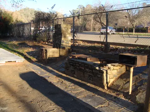 An outdoor stone barbecue pit sits near a chain-link fence.
