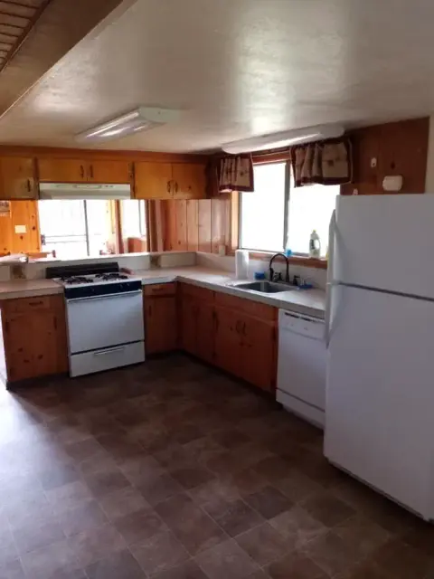 An indoor view of a kitchen with wooden cabinets and white appliances.