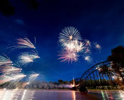 Fireworks display over a river with a bridge.