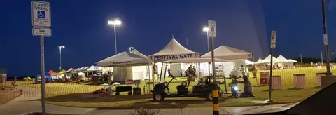 A row of white tents and a golf cart are set up on a grassy field at night.