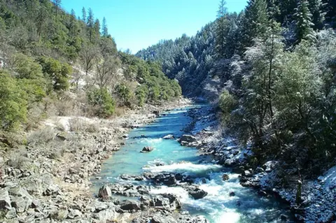 A river flows through a rocky canyon surrounded by forest and light snow.