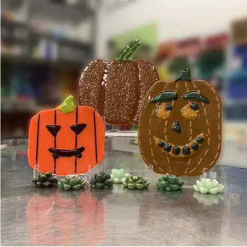 Three fused glass pumpkins are displayed on a tabletop with small decorative succulent figures.
