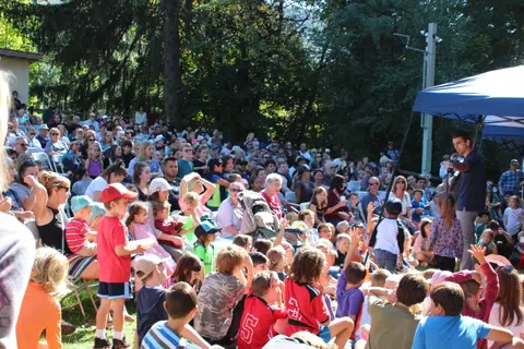 A large crowd of people gathers outdoors to watch a presentation.