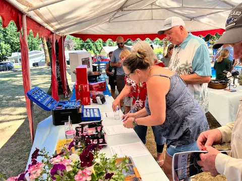 People stand around a table with tools and papers under an outdoor tent.