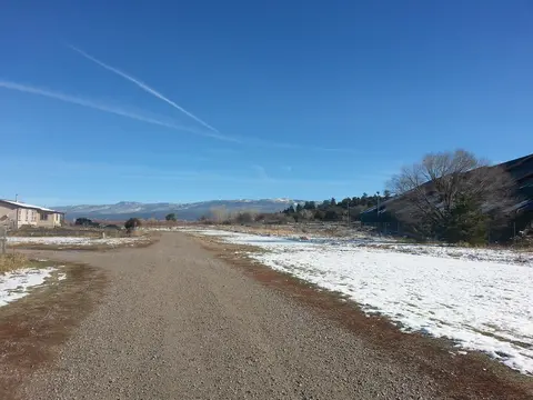 A dirt road leads through a snowy field toward distant mountains under a blue sky.