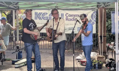 Three musicians performing music under a tent outdoors.
