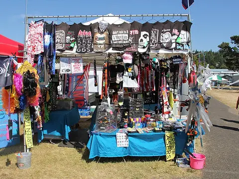 A vendor booth at an outdoor event displaying merchandise like t-shirts, hats, and novelty items.