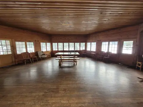 An interior view of a wooden cabin with multiple windows and a table in the center.