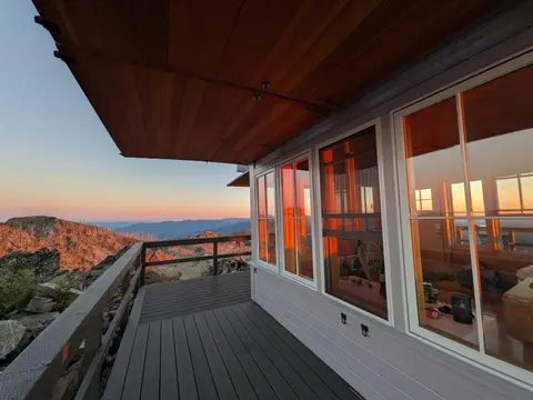 A view from the wooden deck of a building overlooking a mountainous landscape at sunset.