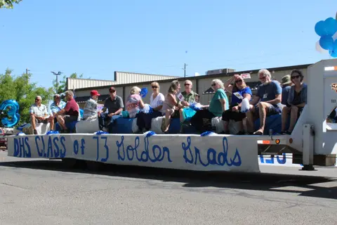 People ride on a parade float with a banner reading DHS Class of '73 Golden Grads.