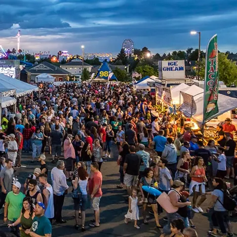 A large crowd of people attending an evening festival outdoors.