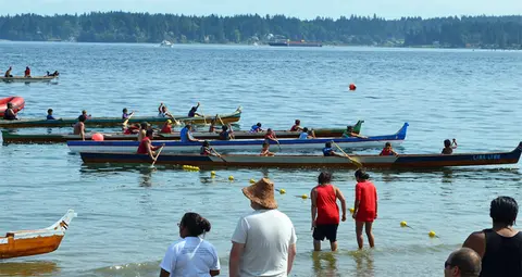 People in canoes on the water and standing on the shore.