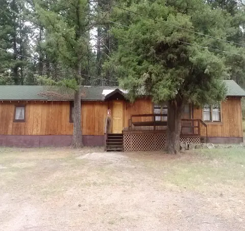 A long wooden cabin stands surrounded by tall trees.