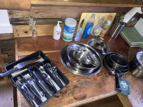 Kitchen items and cleaning supplies on a wooden counter inside a cabin.