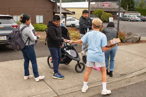A group of people standing outside near cars and a stroller.