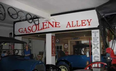 An indoor museum exhibit titled Gasolene Alley features vintage cars and signs.