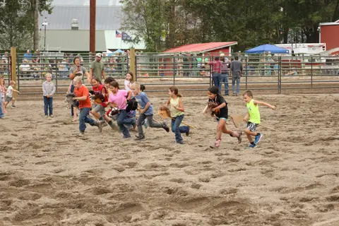 Children participate in a hobby horse race in a dirt arena.