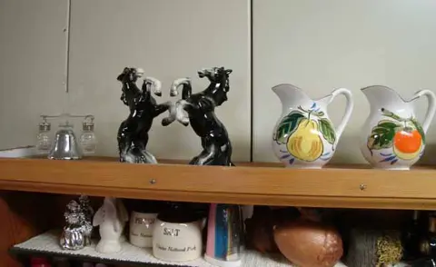 A photograph shows a shelf displaying various ceramic figurines and pitchers.