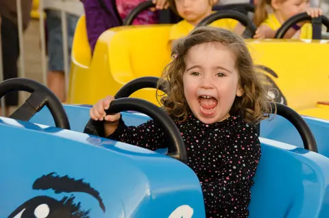 A young girl smiling and shouting happily while riding a carnival ride.
