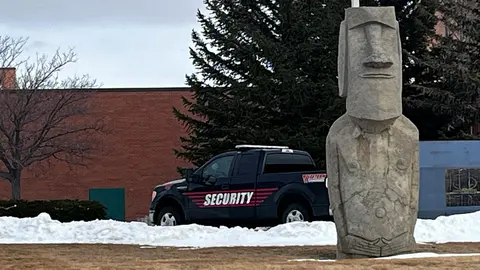 A security truck is parked outdoors near a stone statue in winter.