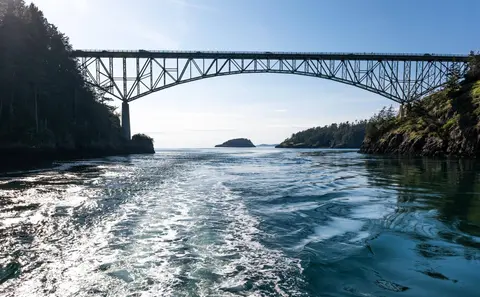 A large arched bridge spans across water between forested cliffs.